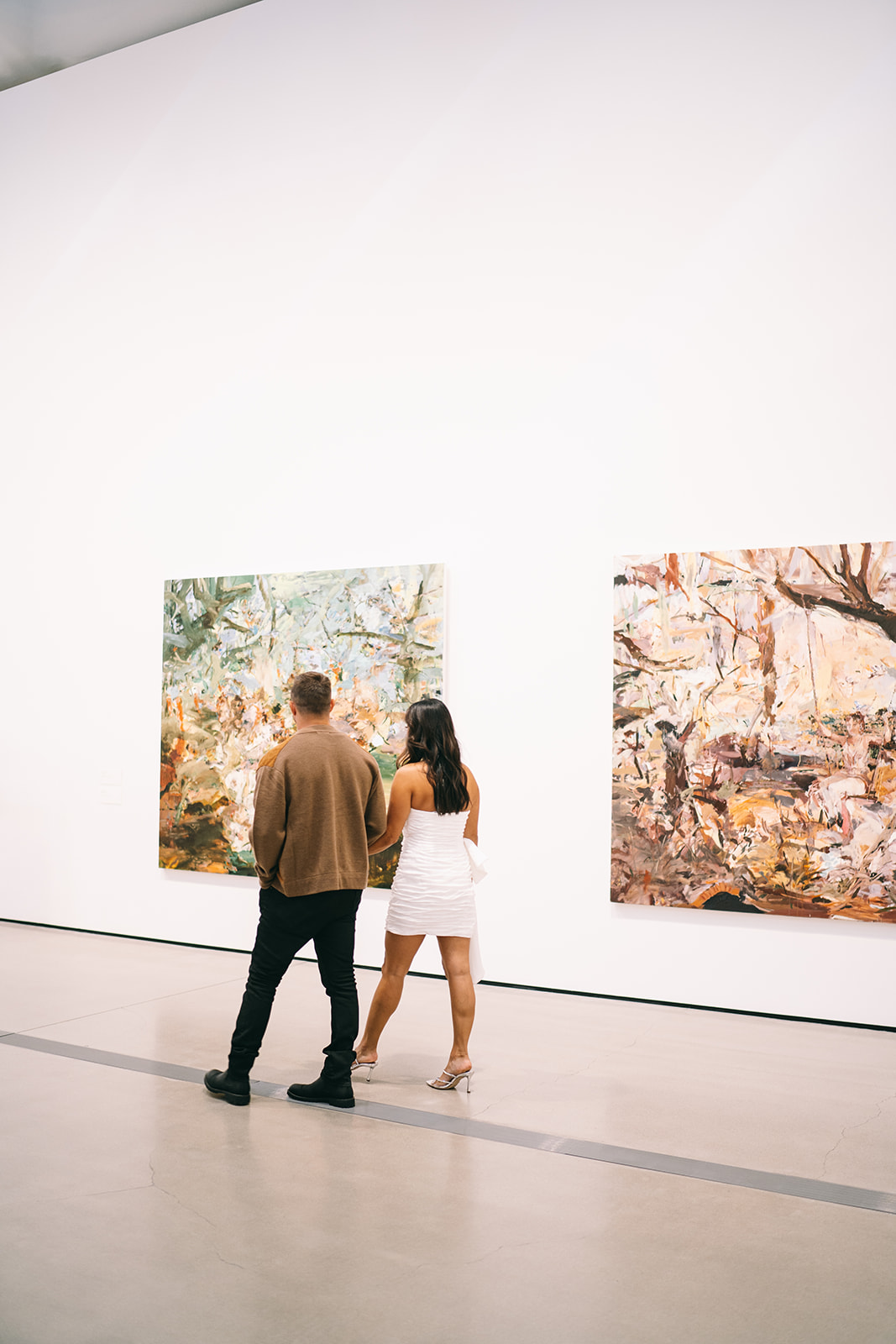 Couple walking through art gallery with two paintings and tall white walls