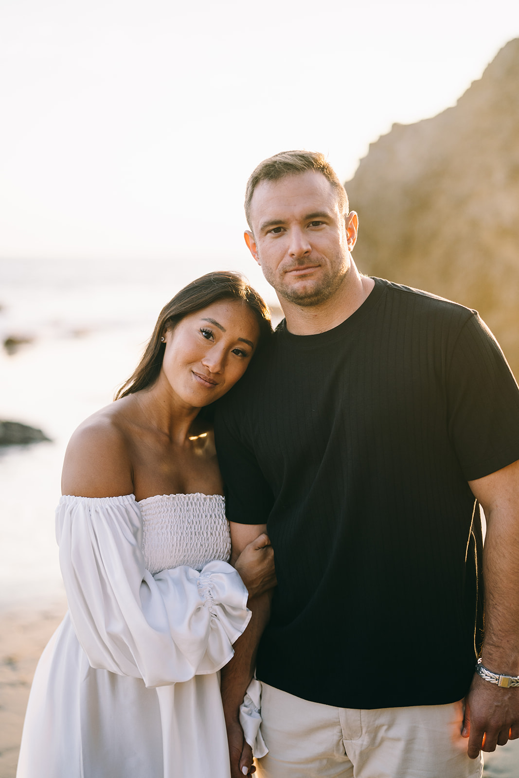 Close up of woman in white and man in black shirt looking into camera being thoughtful malibu engagement