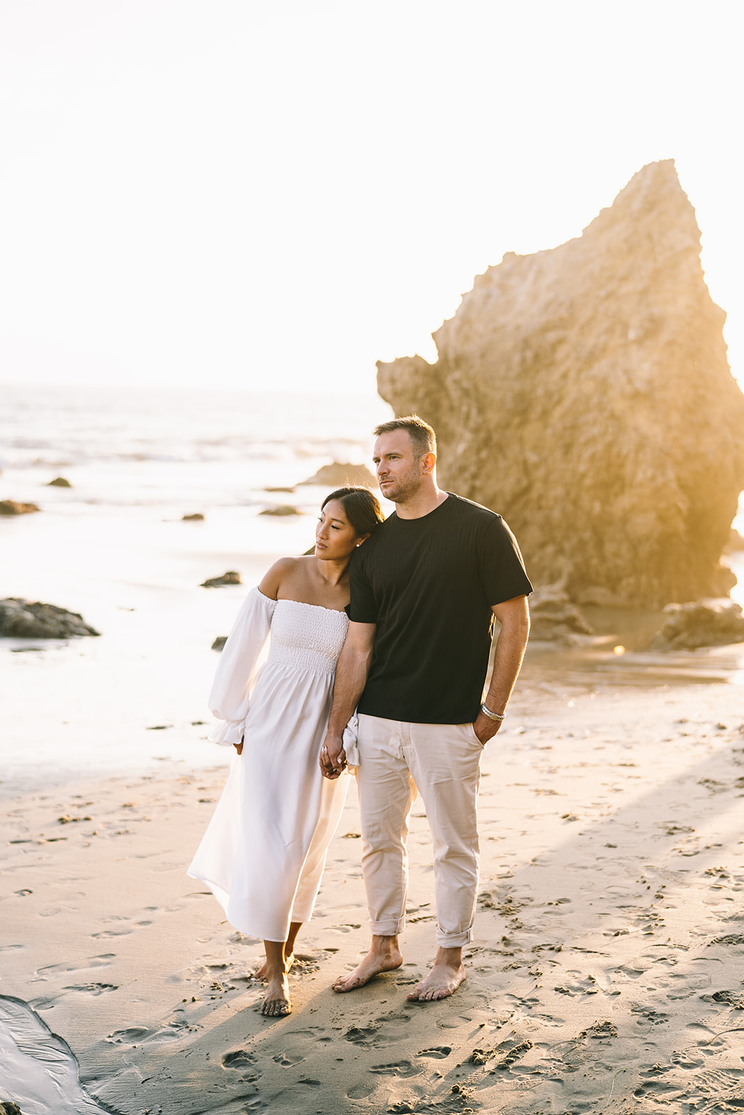 Couple backlit by the sunset on the beach looking off into the distance 