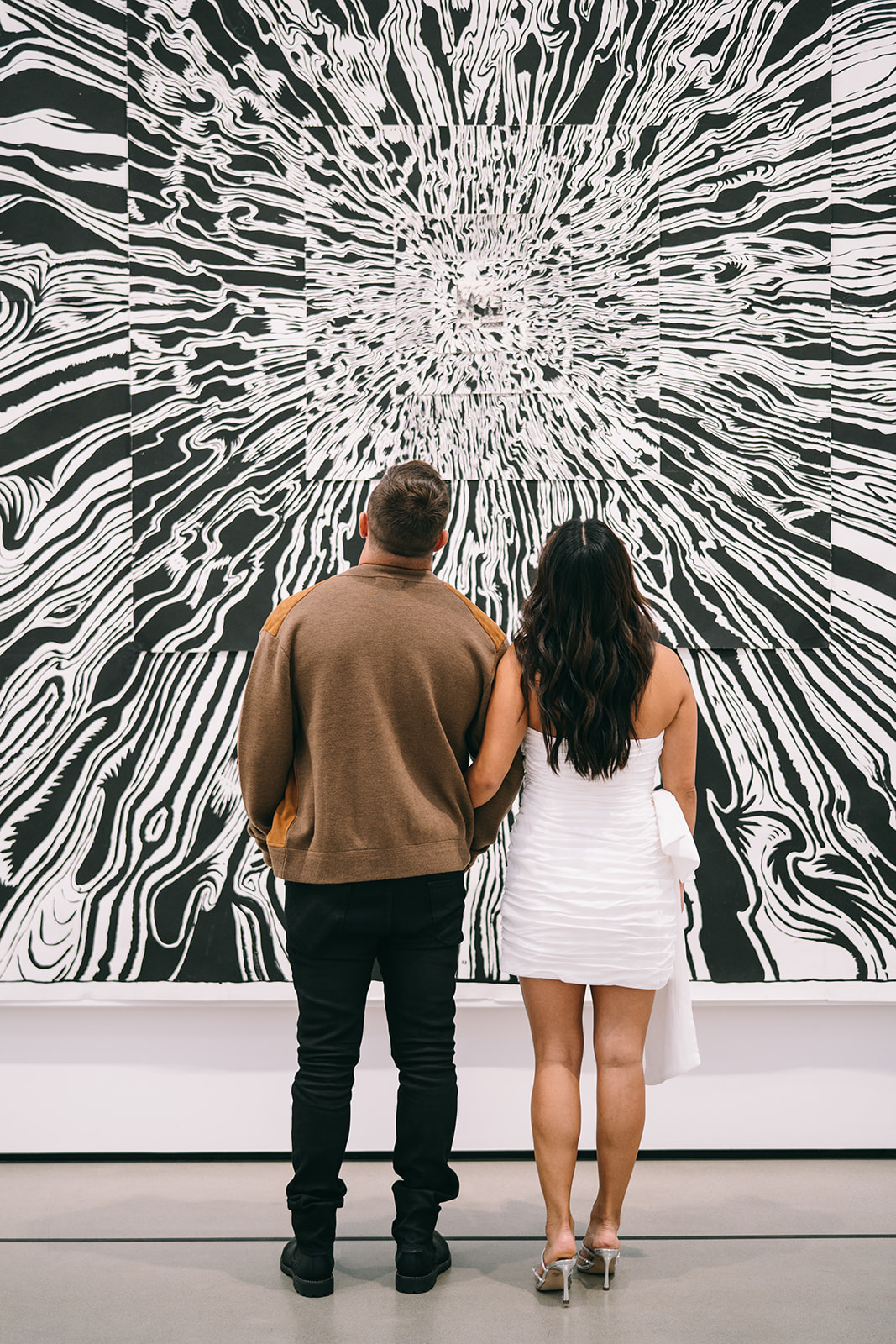 Couple with linked arms looking at a black and white art piece in gallery