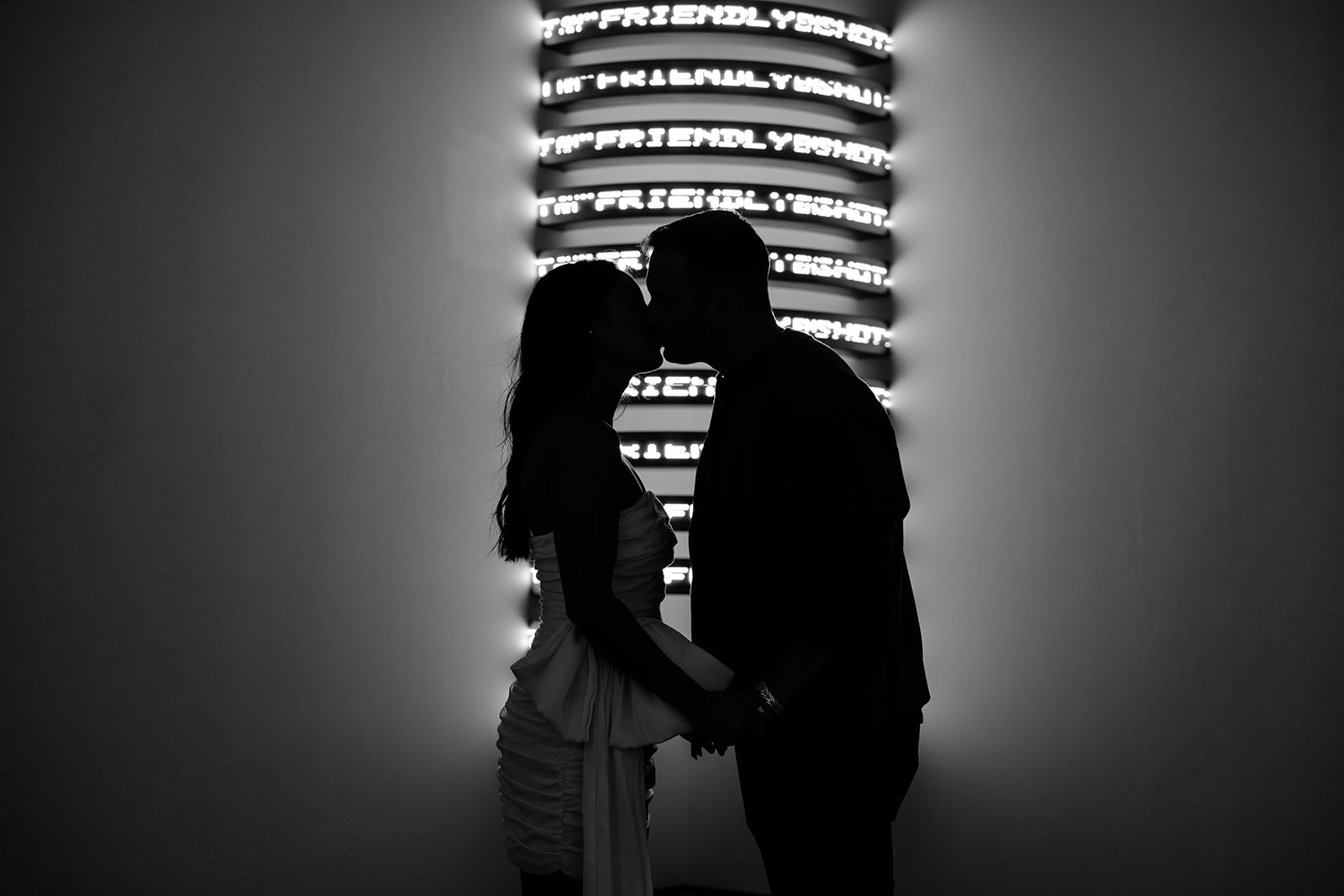 Man and woman kissing in front of an illuminated column with dark background 