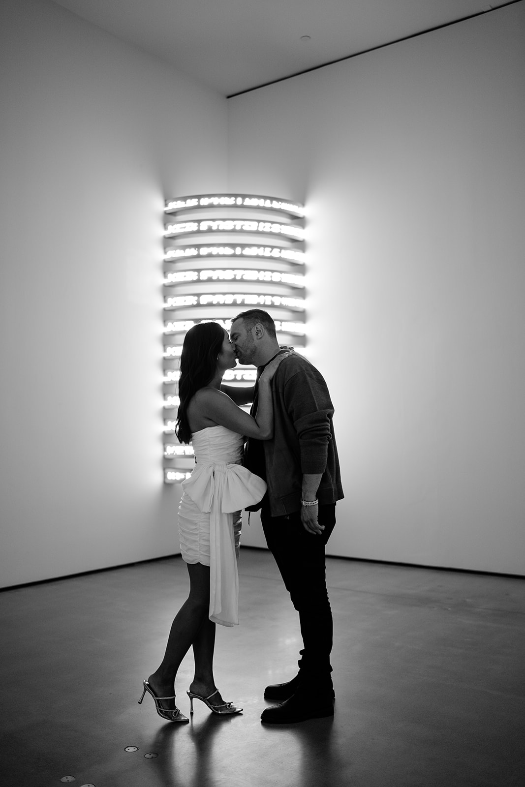 Woman kissing man in front of a corner art instalating that is lit up that has white walls