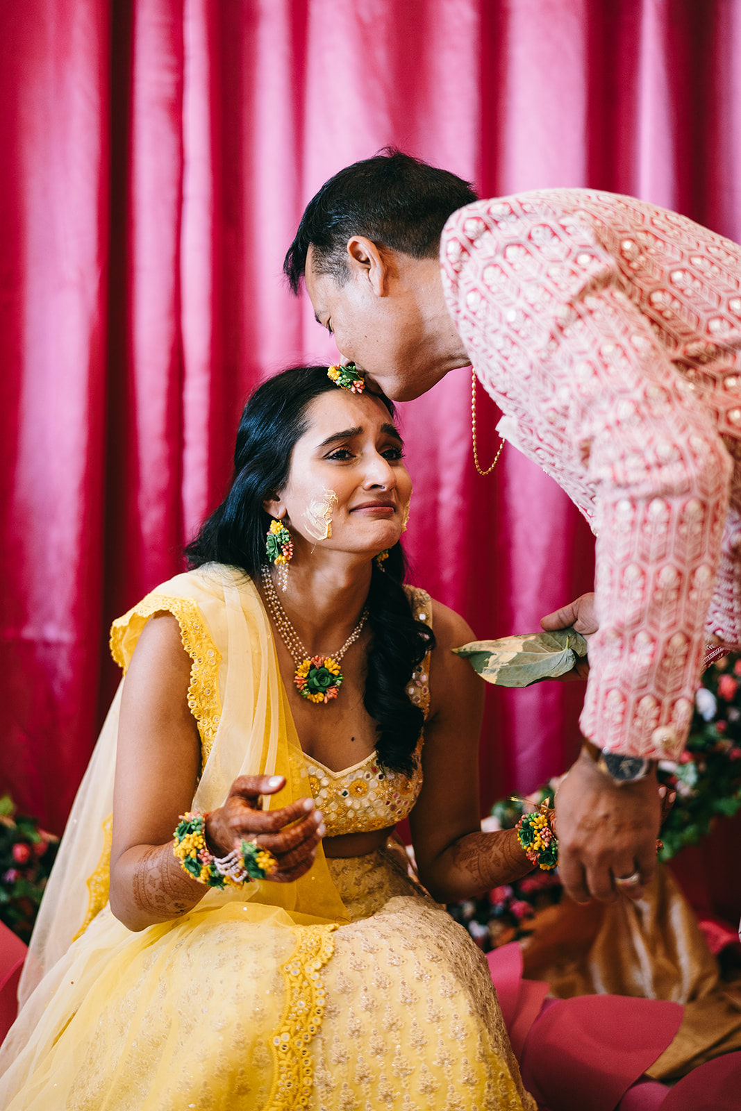 Emotional Indian bride in yellow dress receiving a kiss on her forehead 
