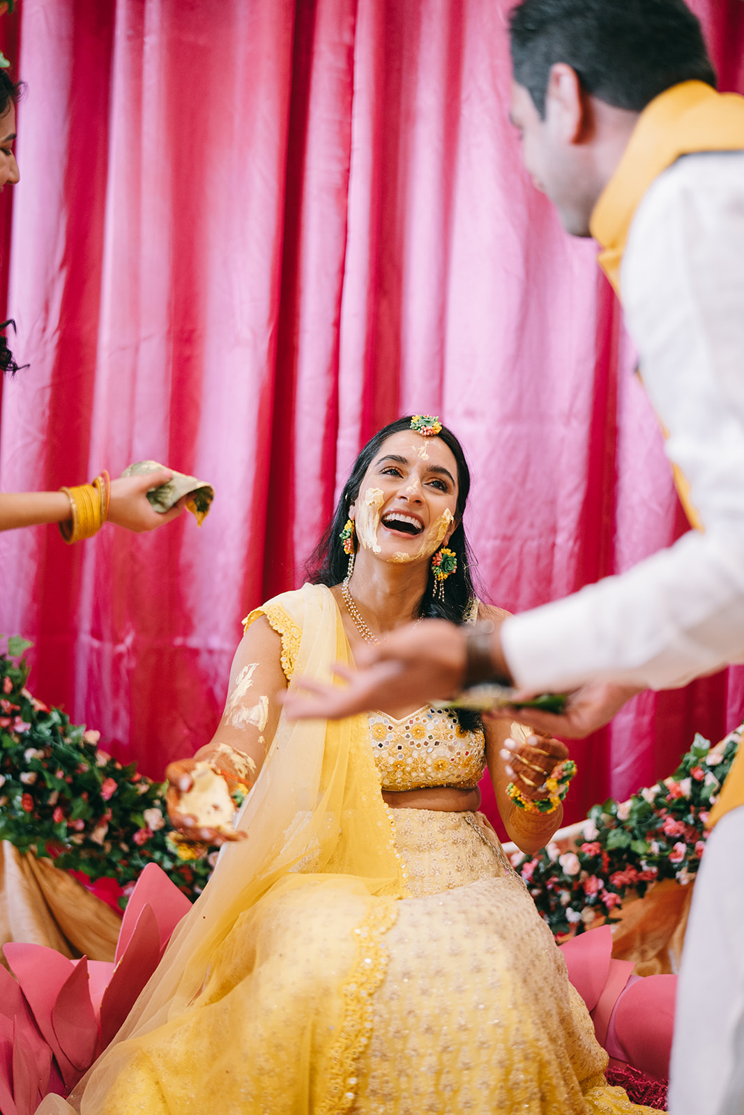 bride sitting in front of pink background in yellow dress looking at her husband and smiling