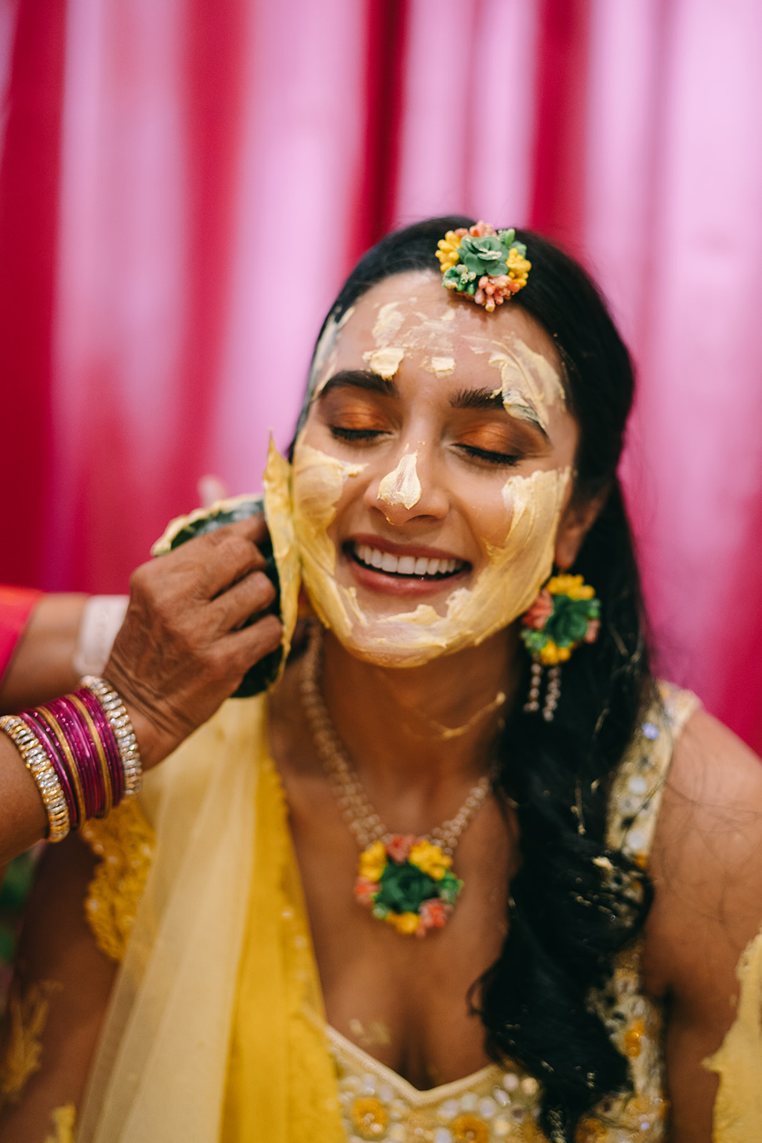 Indian woman in wedding saari smiling as woman applies mask to her face