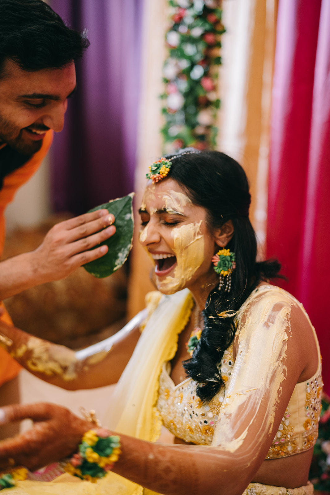 Woman laughing as man applies haldi to her face