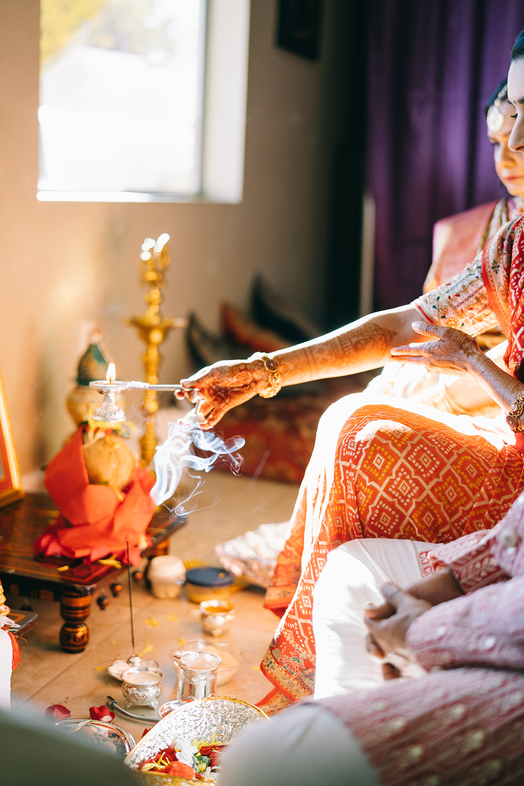 Indian wedding ceremony where bride is holding a candle with incense burning in background