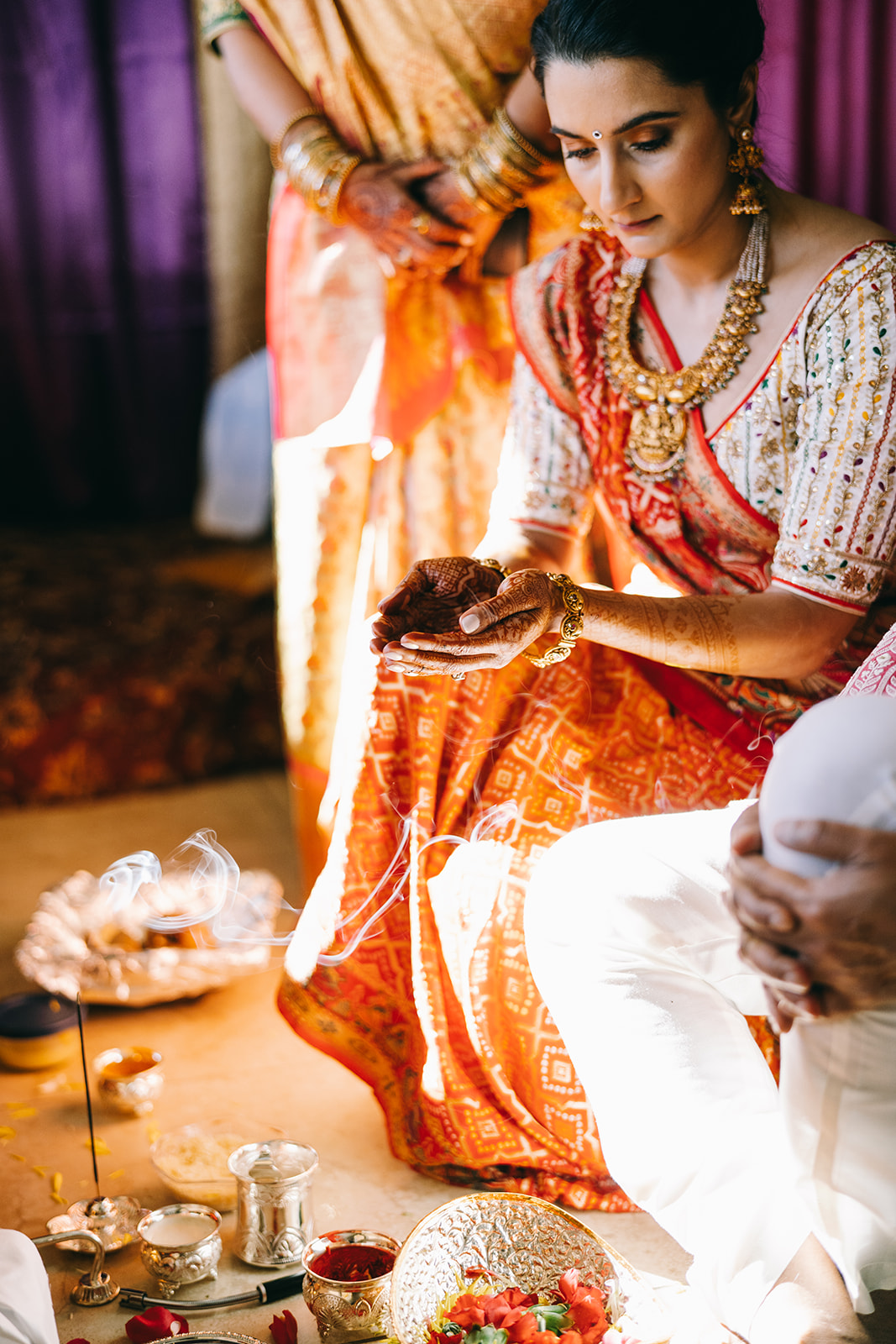 woman in orange saari kneeling with open palms to baskets of flowers