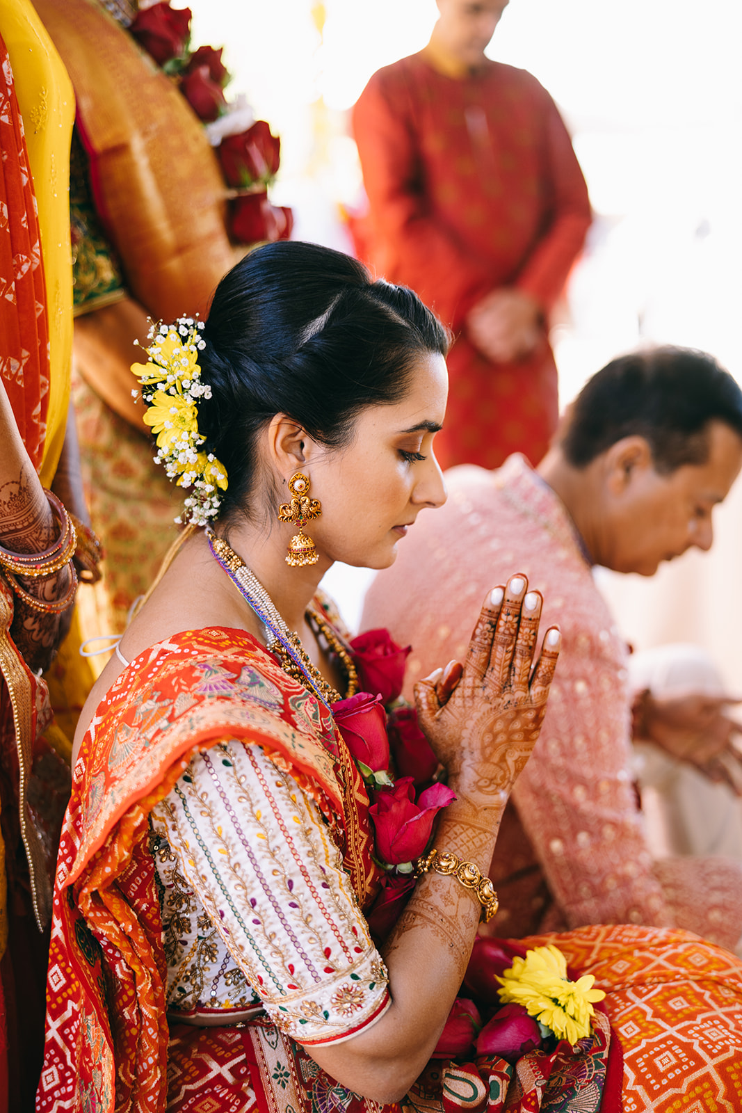 Woman in orange saari with eyes closed and praying hands covered in Henna