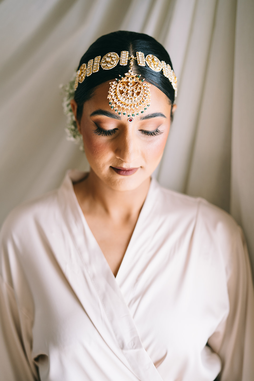 Bride in robe wearing full makeup and a golden headress looking down