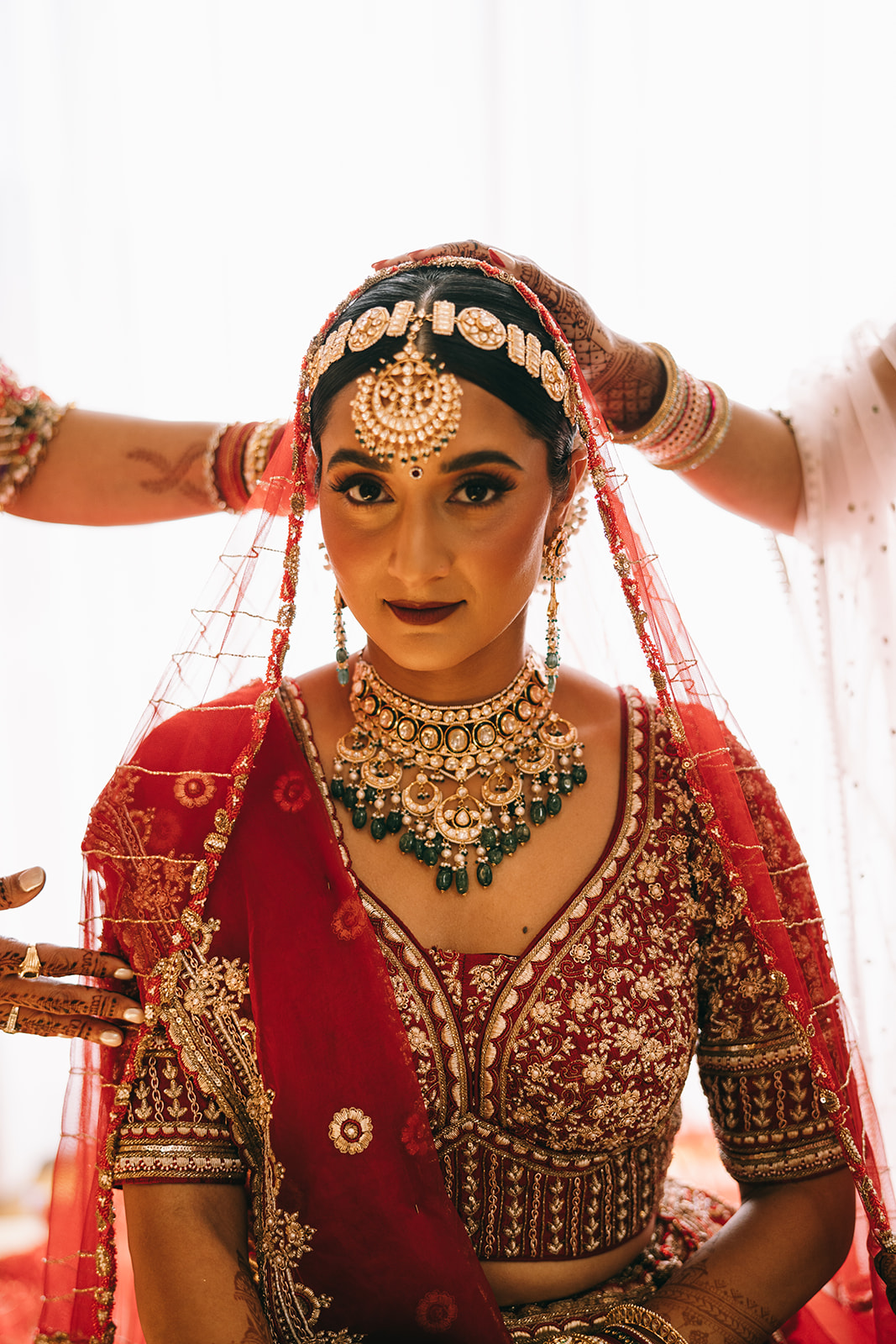 Bride in gold and red dress and golden jewelry and headress looking into the camera smiling slightly