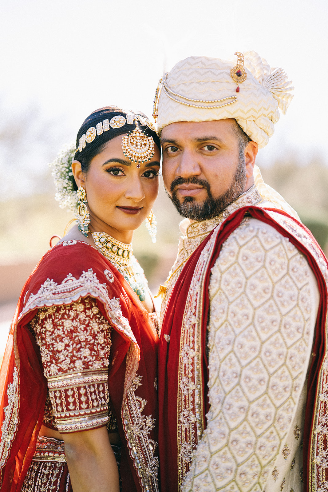 Indian bride and groom standing with their chests facing each other and their faces looking at the camera
