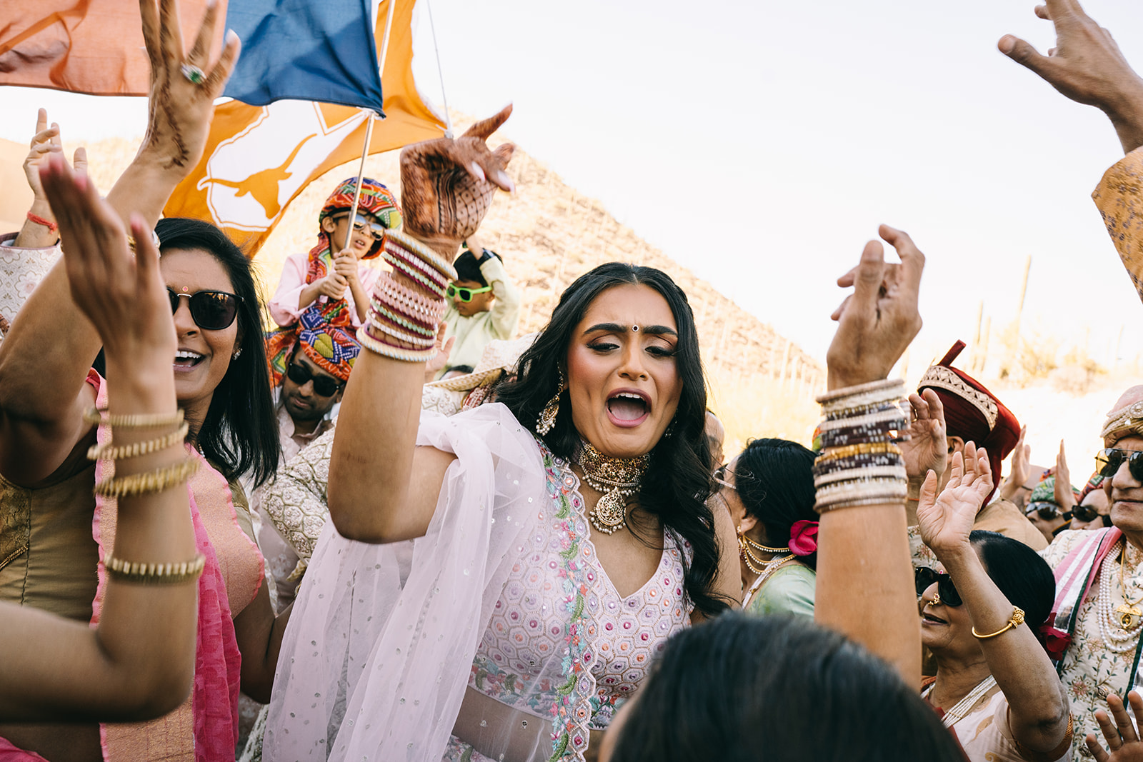 Woman in pink saari being excited with her hands in the air surrounded by people 