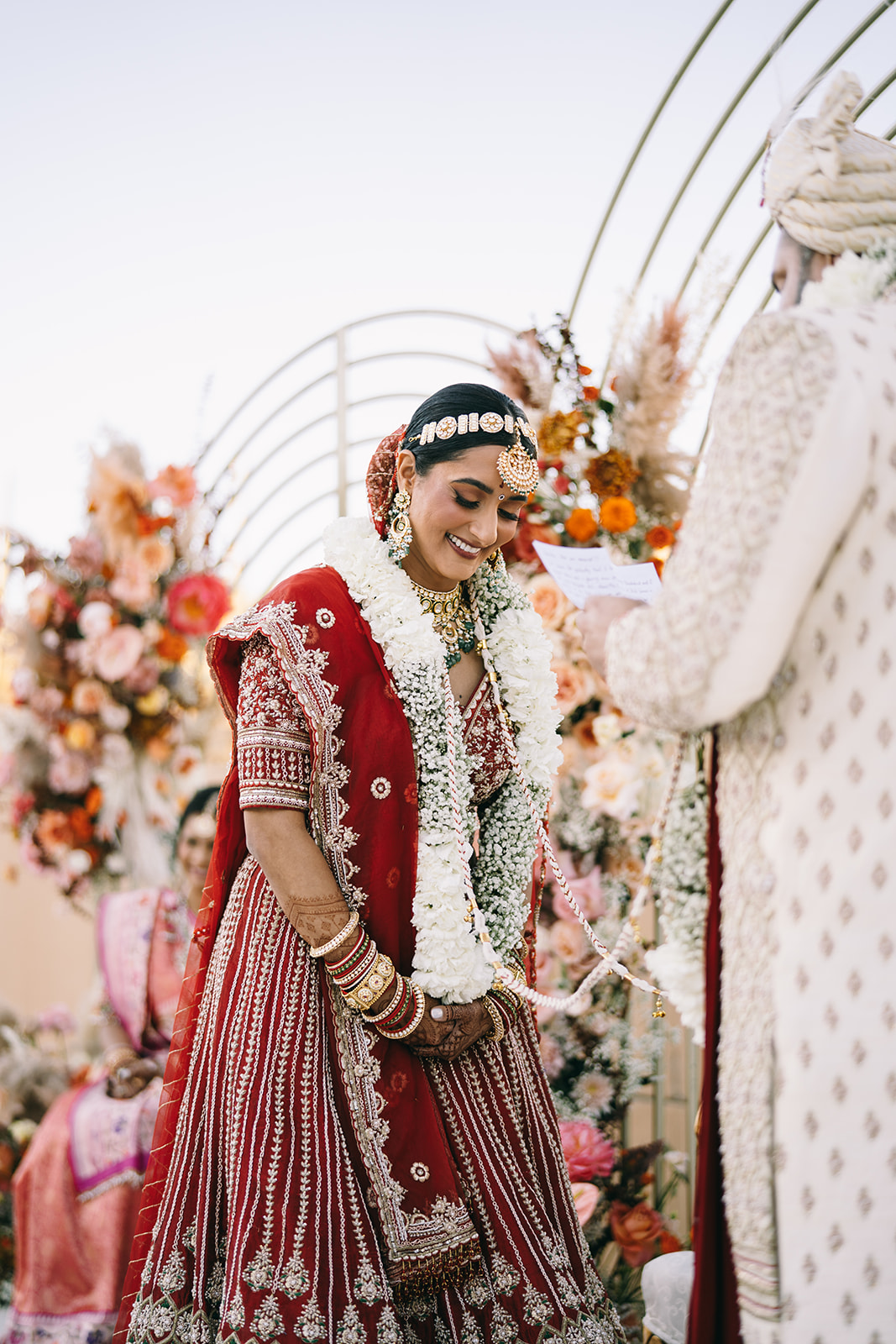 Indian bride in red and gold dress smiling and looking down 