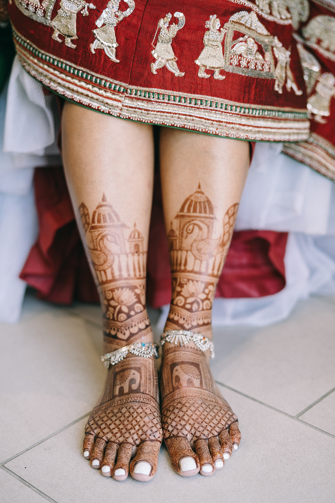 Woman's feet with white toenail polish and anklet with henna on her feet and legs