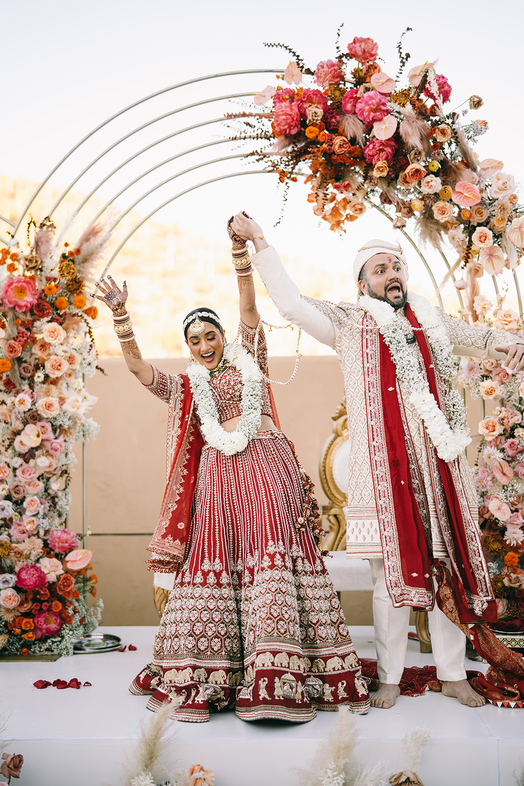 Bride and groom with their hands thrown in the air in celebration under flower arch