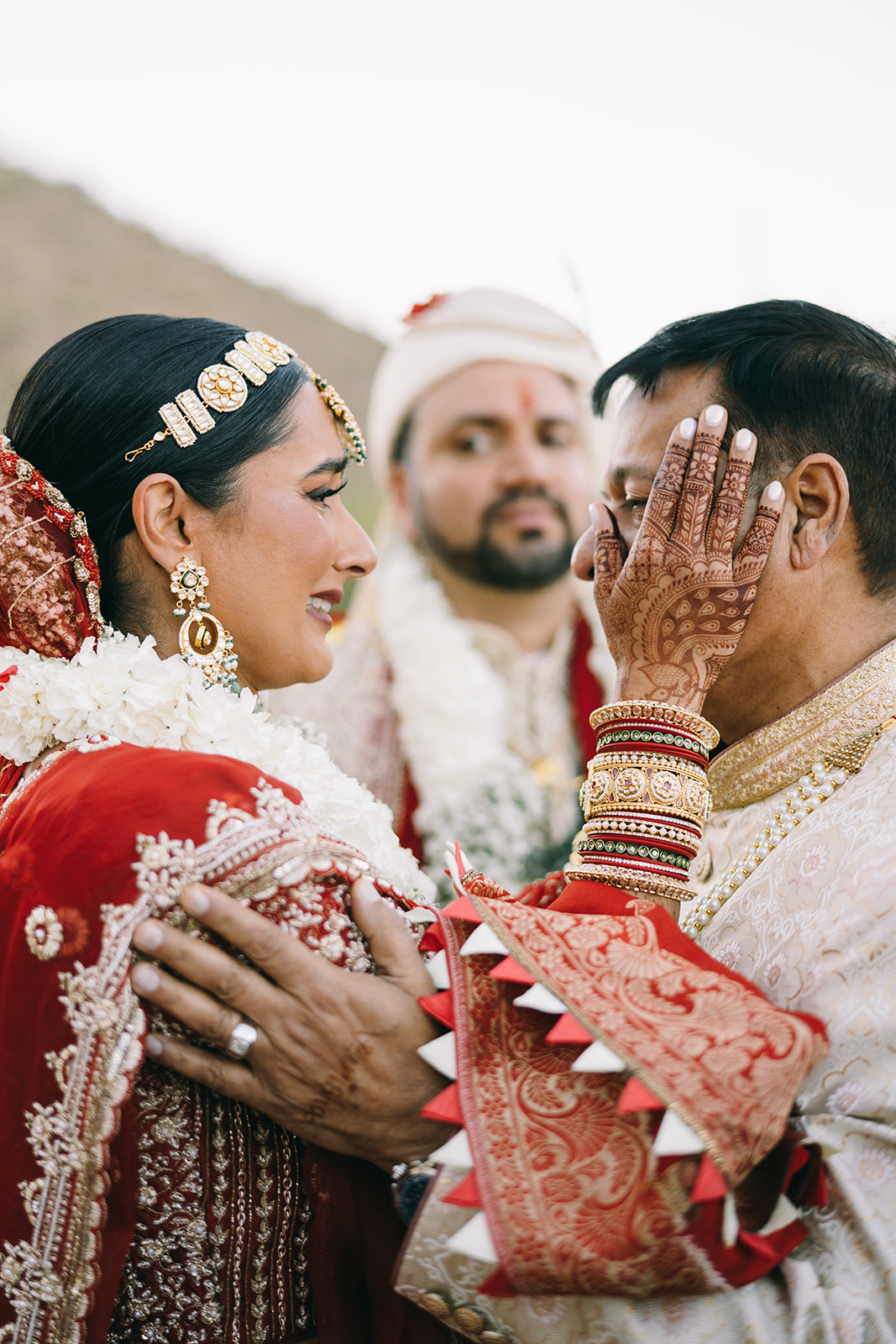 Bride touches elder man's face with tears in her eyes as her husband looks on 