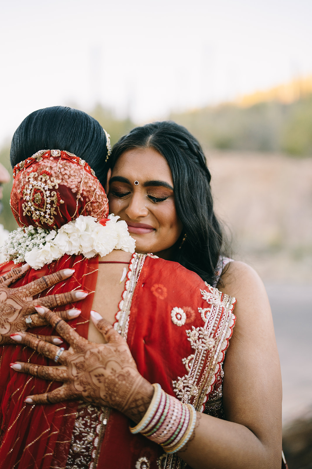 Young indian woman with henna and bangles on her arm embraces bride smiling