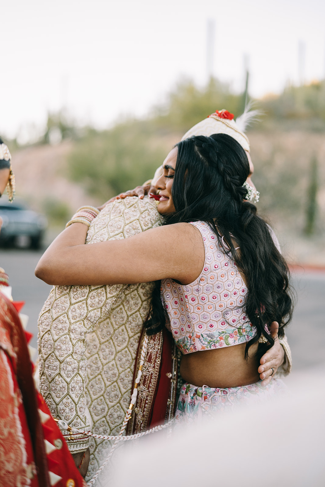 Woman in pink saari embracing man in gold and red wedding attire and crying