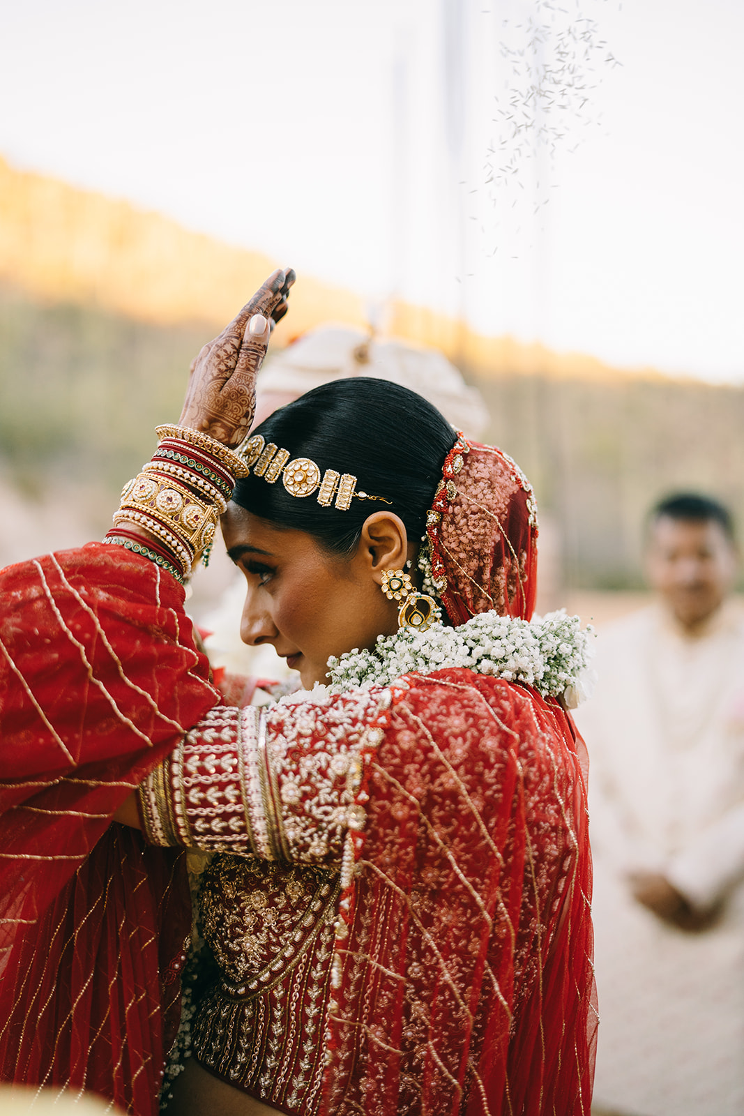 Side profile of indian Bride putting her wrist to her forehead. She has henna and bangles on her arm