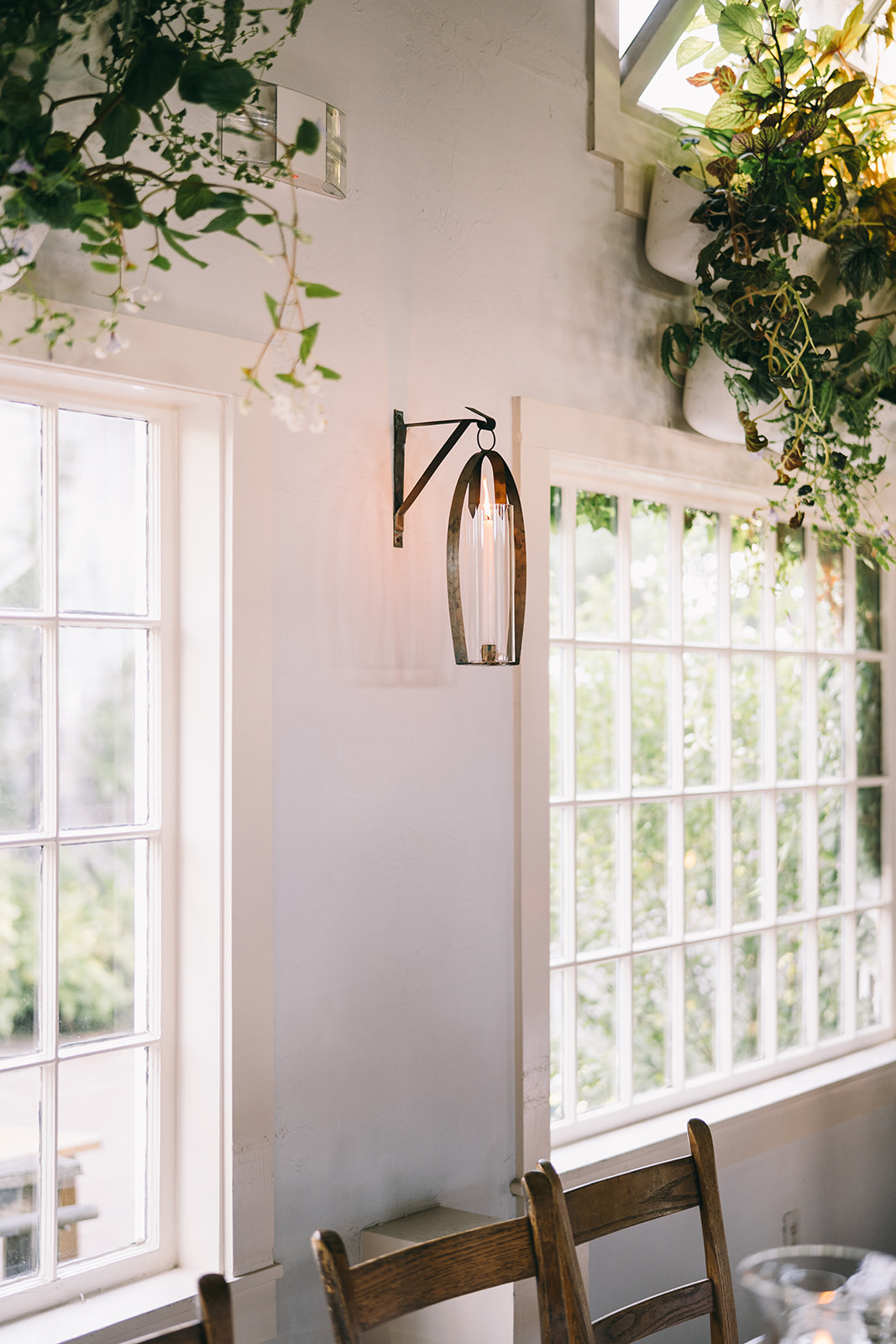 Open windows behind a table with wooden chairs and plants above the windows