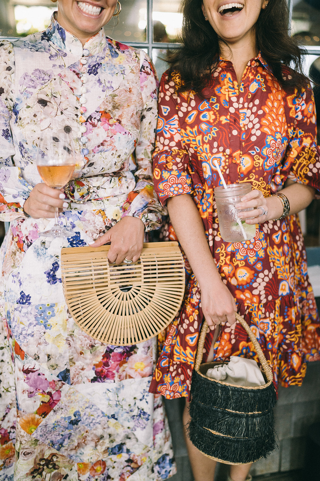 Women in colorful, flowery dresses holding drinks laughing at the camera