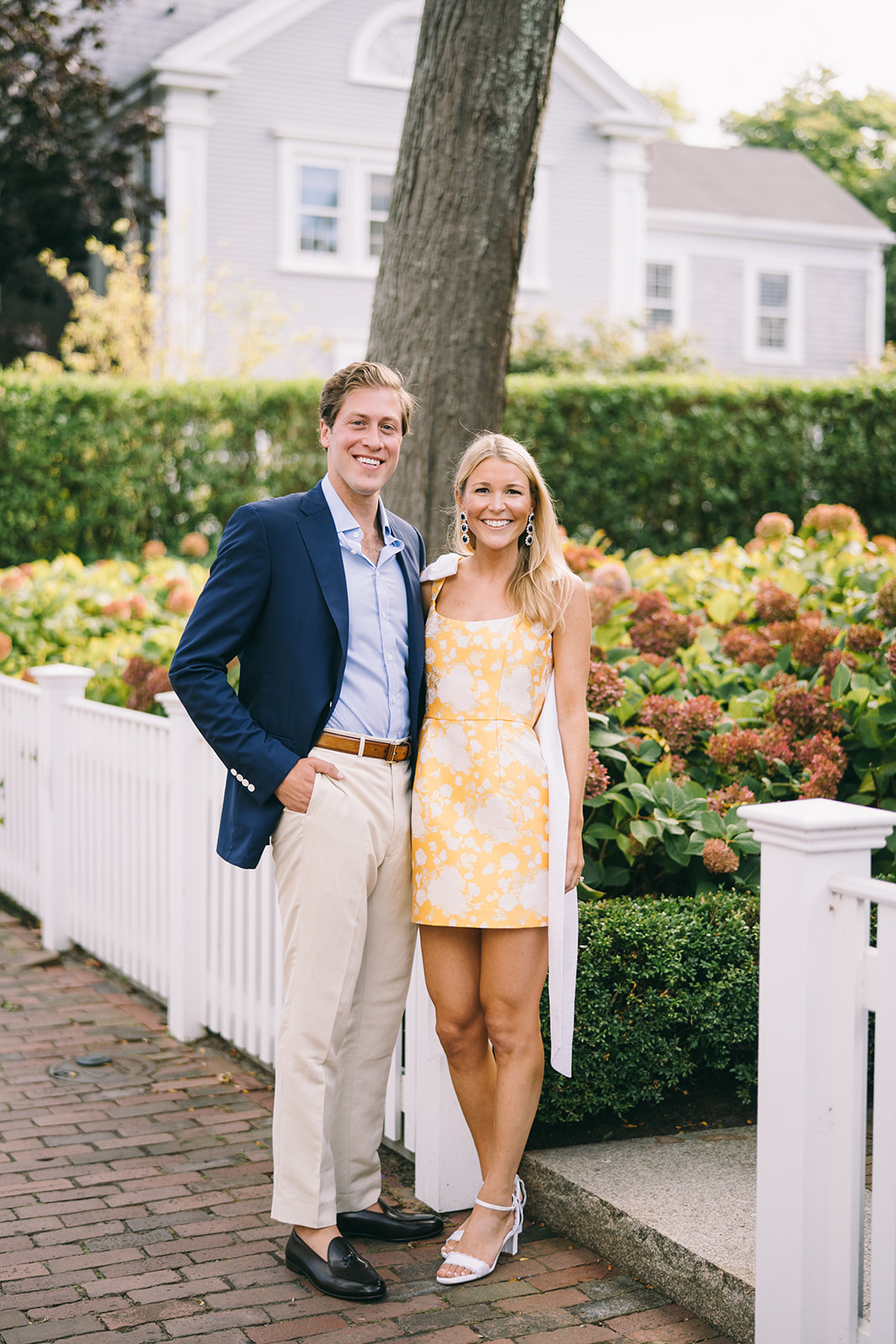 Woman in yellow dress standing with man in khaki slacks and blue blazer standing in front of hydrangea plants