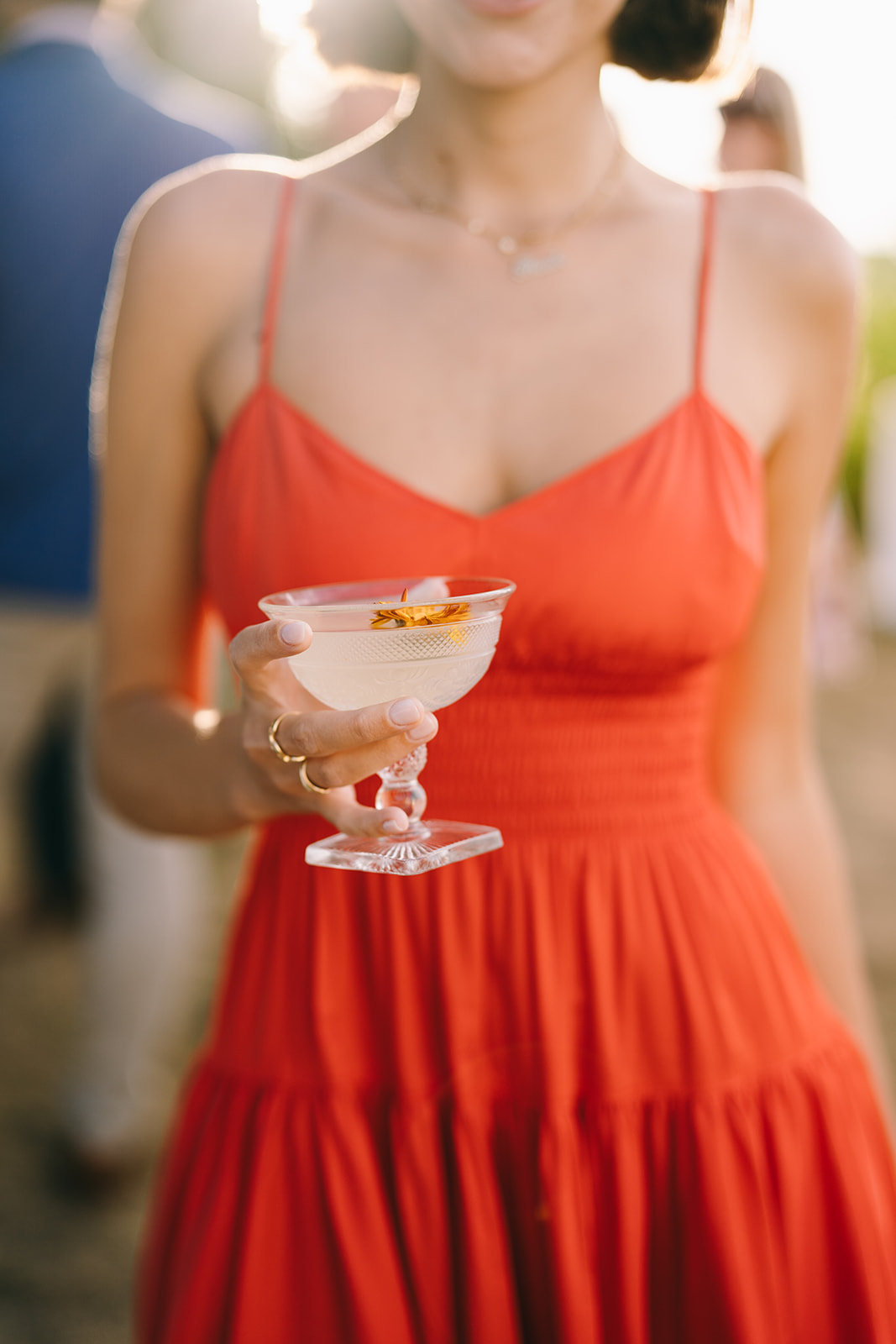 Wedding guests in red orange dress holding a cocktail with the sun setting 